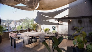 An outdoor patio with a table and chairs, surrounded by potted plants and a view of a cityscape. - Be Living (Vespasiano)