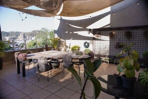 An outdoor patio with a table and chairs, surrounded by potted plants and a view of a cityscape. - Be Living (Vespasiano)