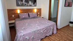 Un dormitorio con cabecera de madera, cama con ropa de cama floral, un cuadro colgado en la pared y una lámpara de techo.