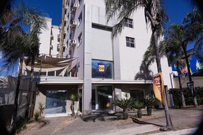 Un edificio moderno con un letrero que dice 'be living', un acceso cubierto y un estacionamiento con palmeras.