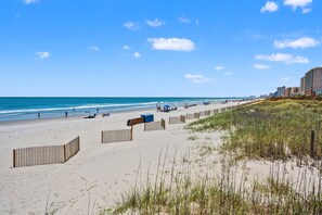 A beach with a wooden fence, beach umbrellas, and a clear sky. - Modern Oceanfront 5BR Home, Private Pool, Elevator, Sleeps 18, Ocean Drive Location (North Myrtle Beach)