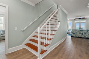 A staircase with white balusters and wooden steps leading to a living area with a view of the ocean. - Modern Oceanfront 5BR Home, Private Pool, Elevator, Sleeps 18, Ocean Drive Location (North Myrtle Beach)