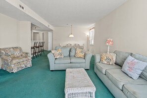 A living room with a sofa set, a patterned armchair, a coffee table, and a dining area with chairs and a table. - Paradise awaits at this elegant marsh condo across street from ocean w/pool, courtyard, sundeck (North Myrtle Beach)