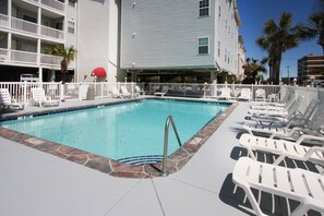 A swimming pool with lounge chairs, a lifeguard stand, and a building with balconies. - Paradise awaits at this elegant marsh condo across street from ocean w/pool, courtyard, sundeck (North Myrtle Beach)