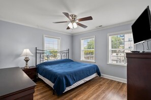 A bedroom with a bed, a desk, a lamp, a ceiling fan, and two windows. - 6BR ocean-view home in Crescent Beach with beach access and parking (North Myrtle Beach)
