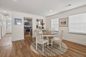 A dining area with a round table and chairs, a kitchen in the background, and a patterned rug on the floor. - 6BR ocean-view home in Crescent Beach with beach access and parking (North Myrtle Beach)