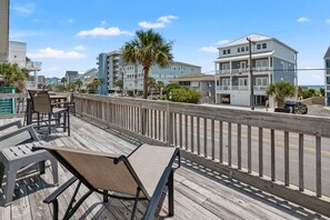 A wooden deck with outdoor seating, overlooking a street with buildings and a clear sky. - 6BR ocean-view home in Crescent Beach with beach access and parking (North Myrtle Beach)