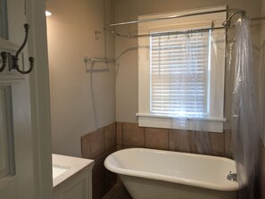 Un baño con bañera, una ventana con persianas y un cortinero.