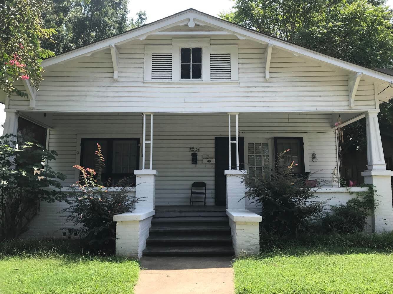 A two-story white house with a front porch, steps leading to the entrance, and a mailbox on the front wall.