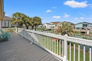 A wooden deck with white railings overlooking a body of water, with houses in the background. - Waterfront channel home close to beach - fishing and crabbing (North Myrtle Beach)