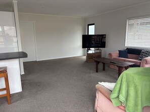 Ein Wohnzimmer mit Flachbildfernseher, einem rosafarbenen Sofa, einem Holztisch und einem kleinen Holzschrank.
