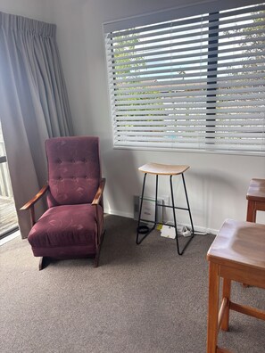 Ein Zimmer mit einem violetten Sessel, einem Holztisch und einem Fenster mit Jalousien.