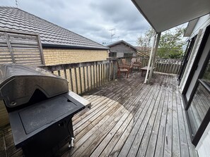Eine Holzterrasse mit Grill, Ziegelwand und Holzzaun.