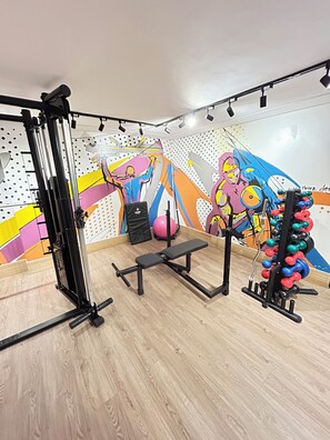 A gym with a bench press, squat rack, and dumbbells. - Melhores Flats - Acolhedor, 30m do mar  (João Pessoa)