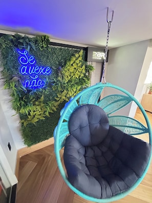 A room with a hanging chair, a neon sign, and a green wall with plants. - Melhores Flats - Acolhedor, 30m do mar  (João Pessoa)