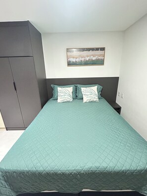 A bedroom with a bed, a nightstand, a wardrobe, and a painting on the wall. - Melhores Flats - Acolhedor, 30m do mar  (João Pessoa)