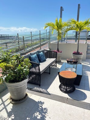 A rooftop terrace with a sofa, chairs, a table, and potted plants. - Melhores Flats - Acolhedor, 30m do mar  (João Pessoa)