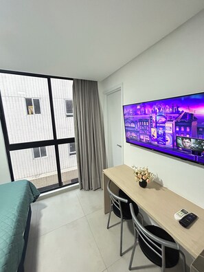 Hotelkamer met een bed, een bureau, een stoel, een raam met gordijnen en een aan de muur bevestigde televisie waarop een stadsgezicht te zien is.