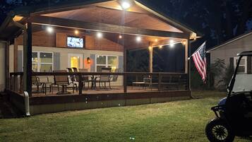 Un espacio de estar al aire libre cubierto, con mesas, sillas, una pantalla de televisión y una bandera estadounidense.