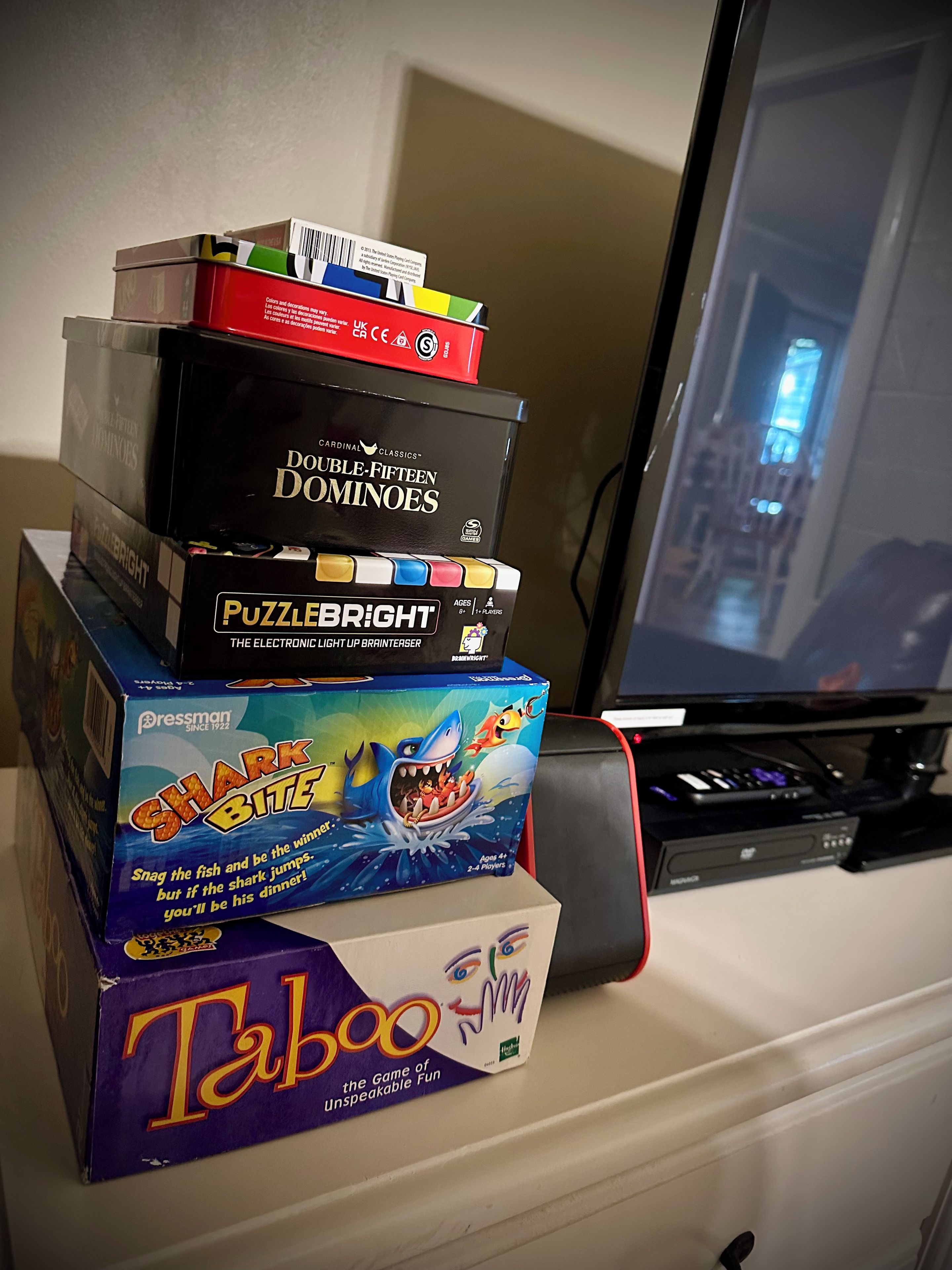 Ein Stapel Brettspiele auf einem Tisch, im Hintergrund ein Computermonitor.