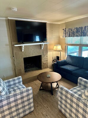 A living room with a fireplace, a flat-screen TV mounted above it, a blue sofa, and plaid-patterned chairs.