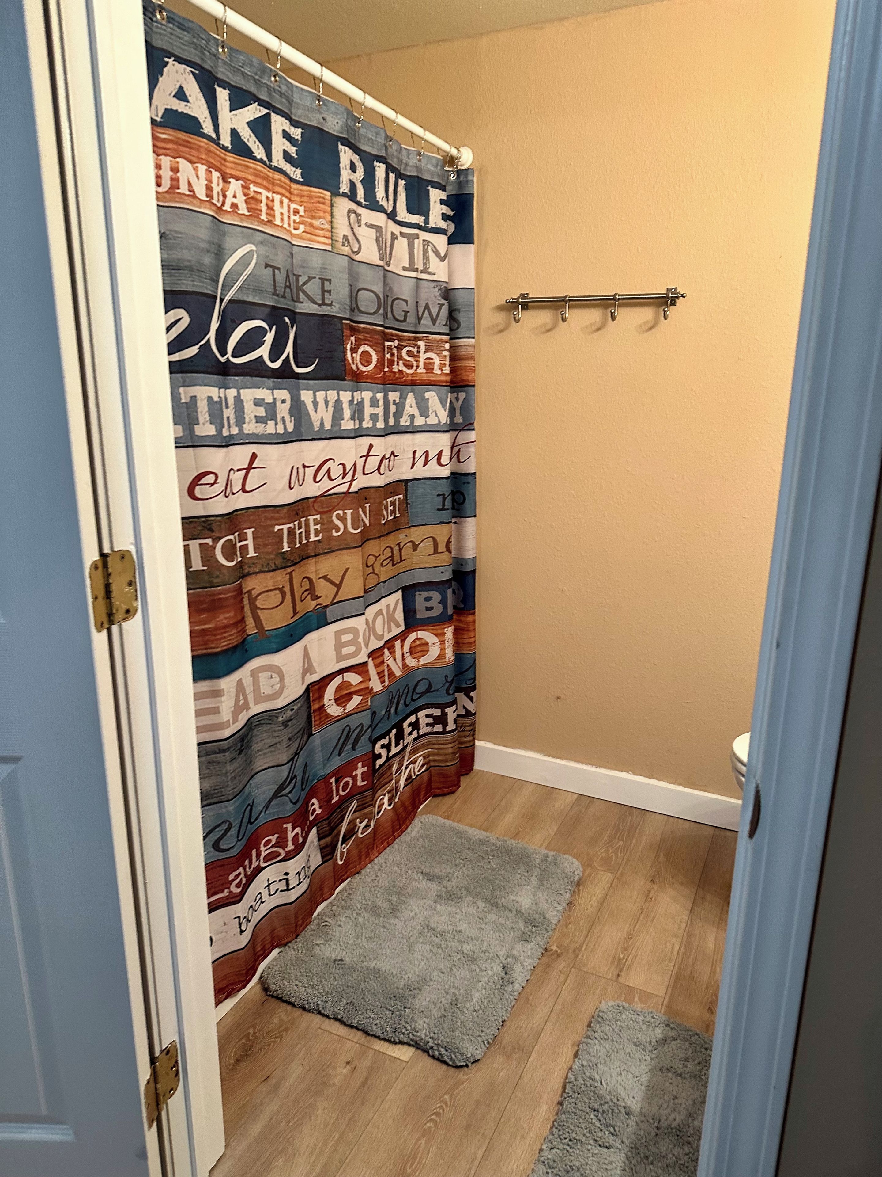 A bathroom with a shower curtain featuring various phrases and a small rug on the floor.