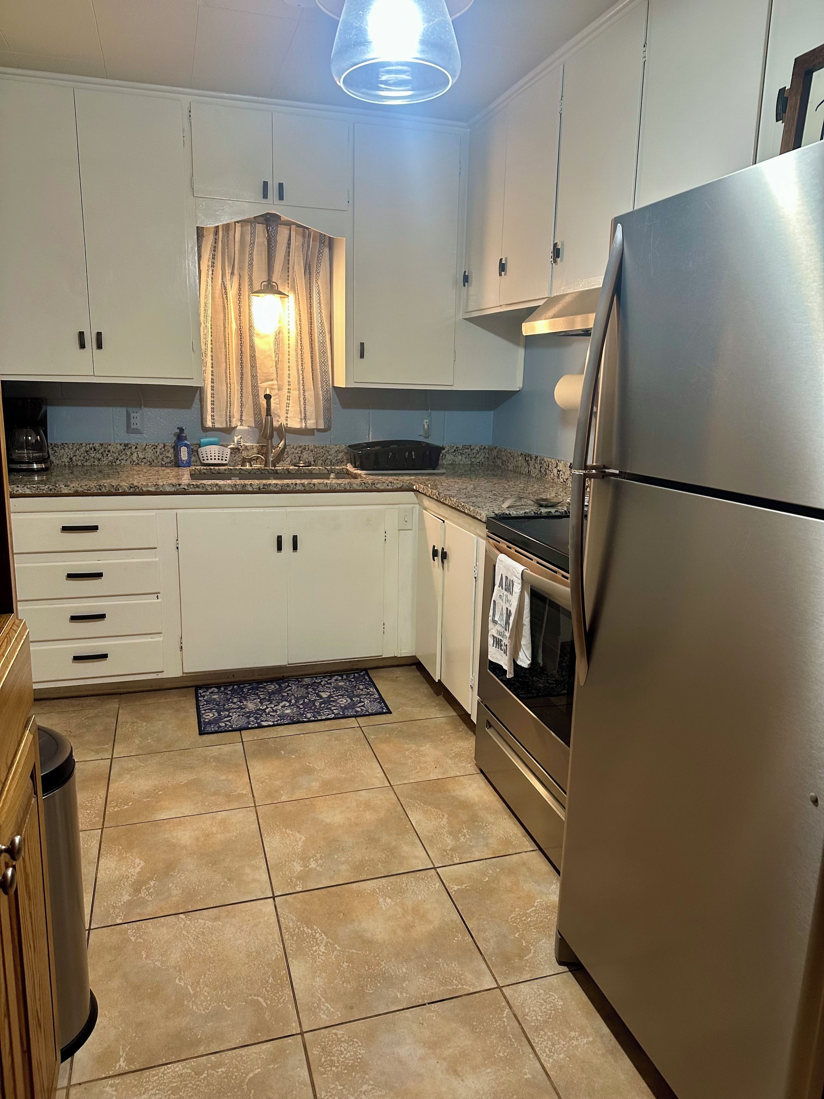 Una cocina con armarios blancos, un refrigerador de acero inoxidable, un lavamanos y una estufa.