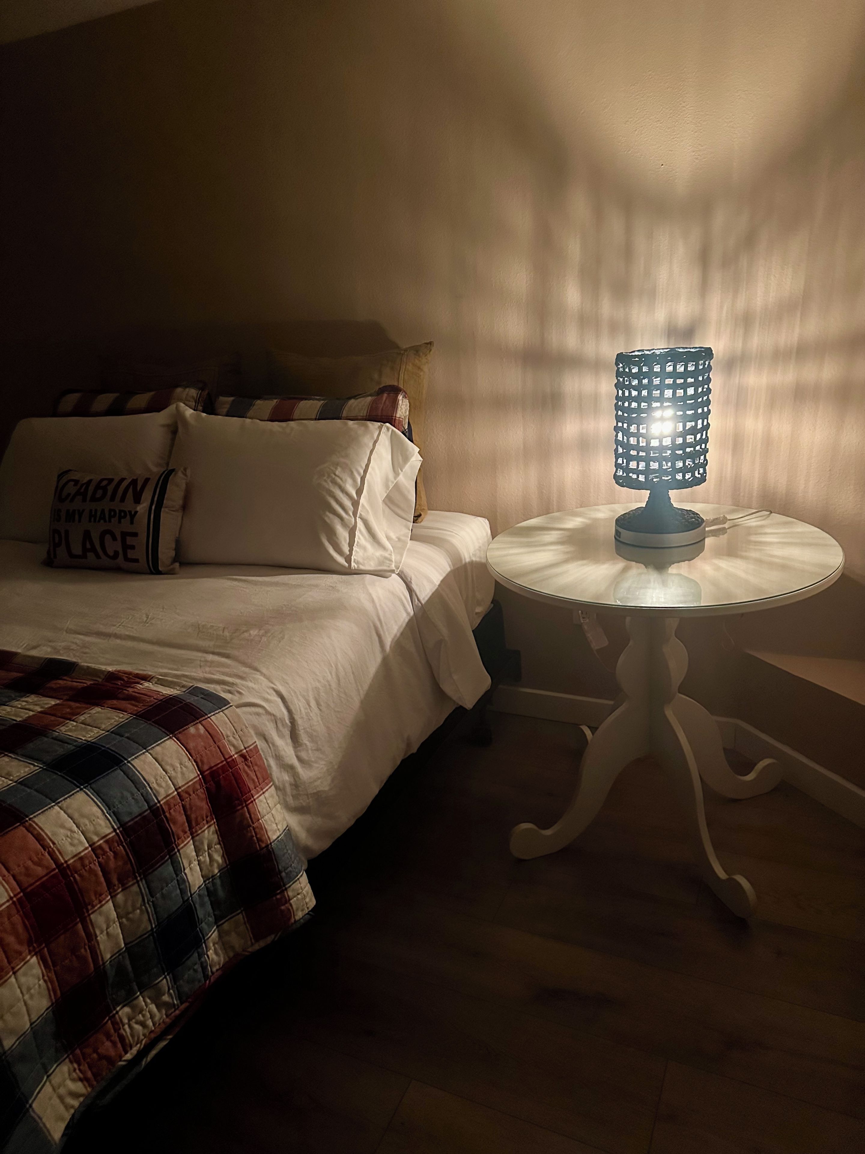 Un dormitorio con una cama, almohadas, una mesita de noche con lámpara y una ventana que ilumina la pared.