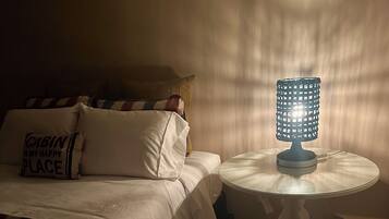 Un dormitorio con una cama, almohadas, una mesita de noche con lámpara y una ventana que ilumina la pared.