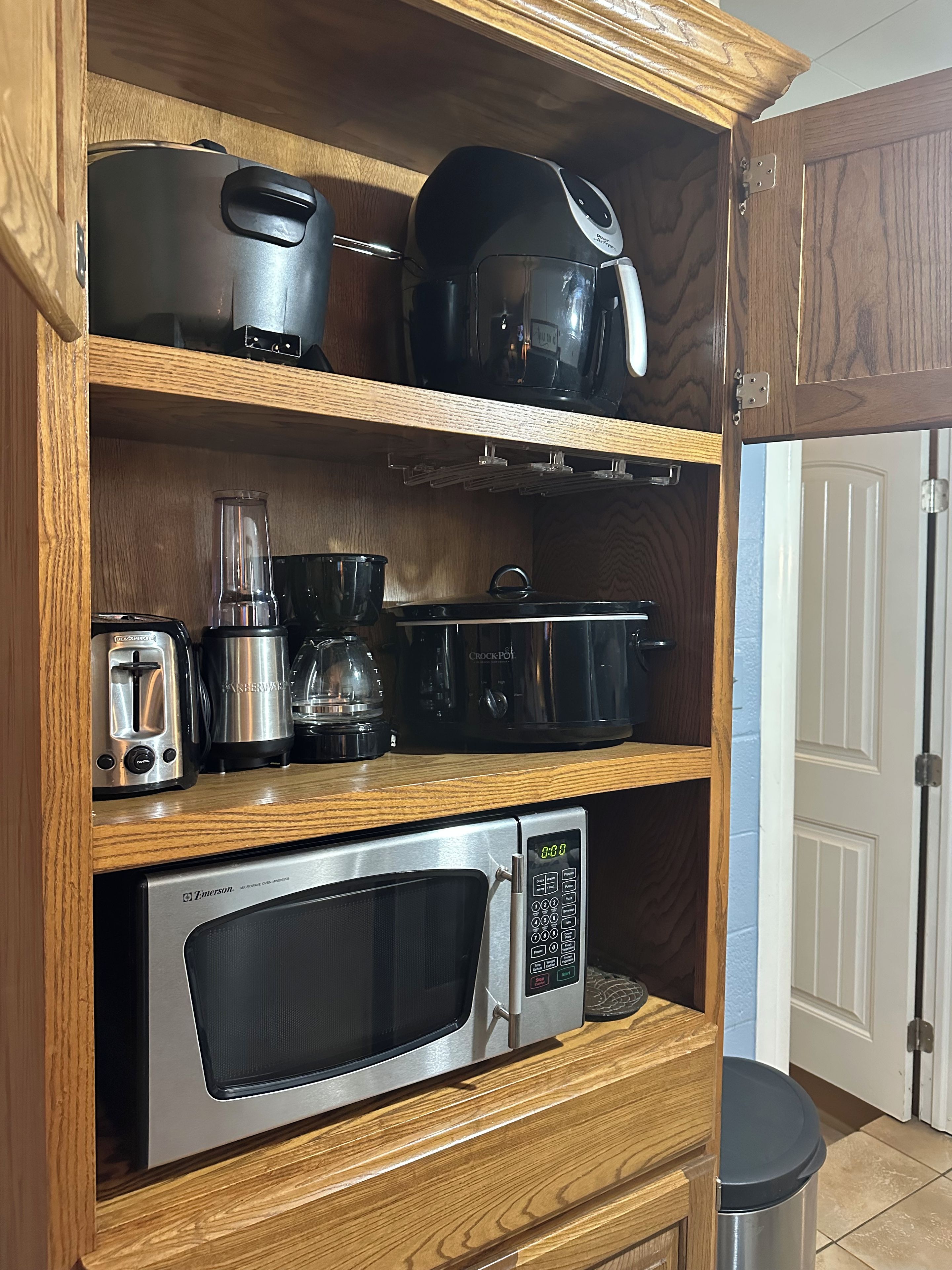 A kitchen with a microwave, toaster, blender, and various appliances on wooden shelves.