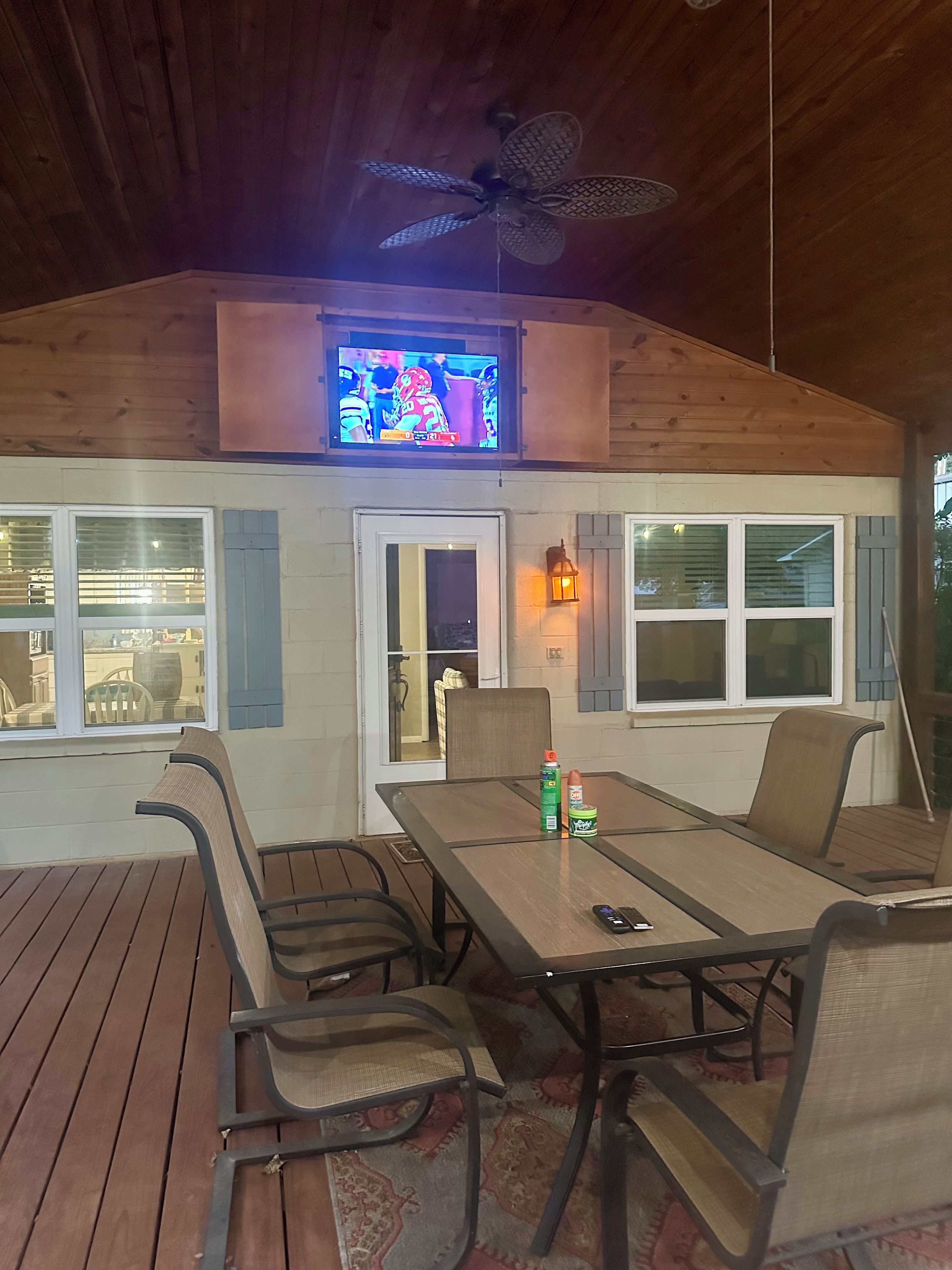 Un patio al aire libre con una mesa, sillas, un ventilador de techo y un televisor sobre la mesa.