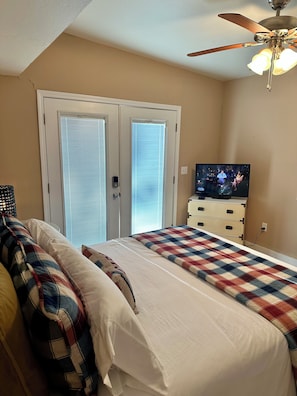 Een slaapkamer met een bed, een televisie, een plafondventilator en een deur met luiken.