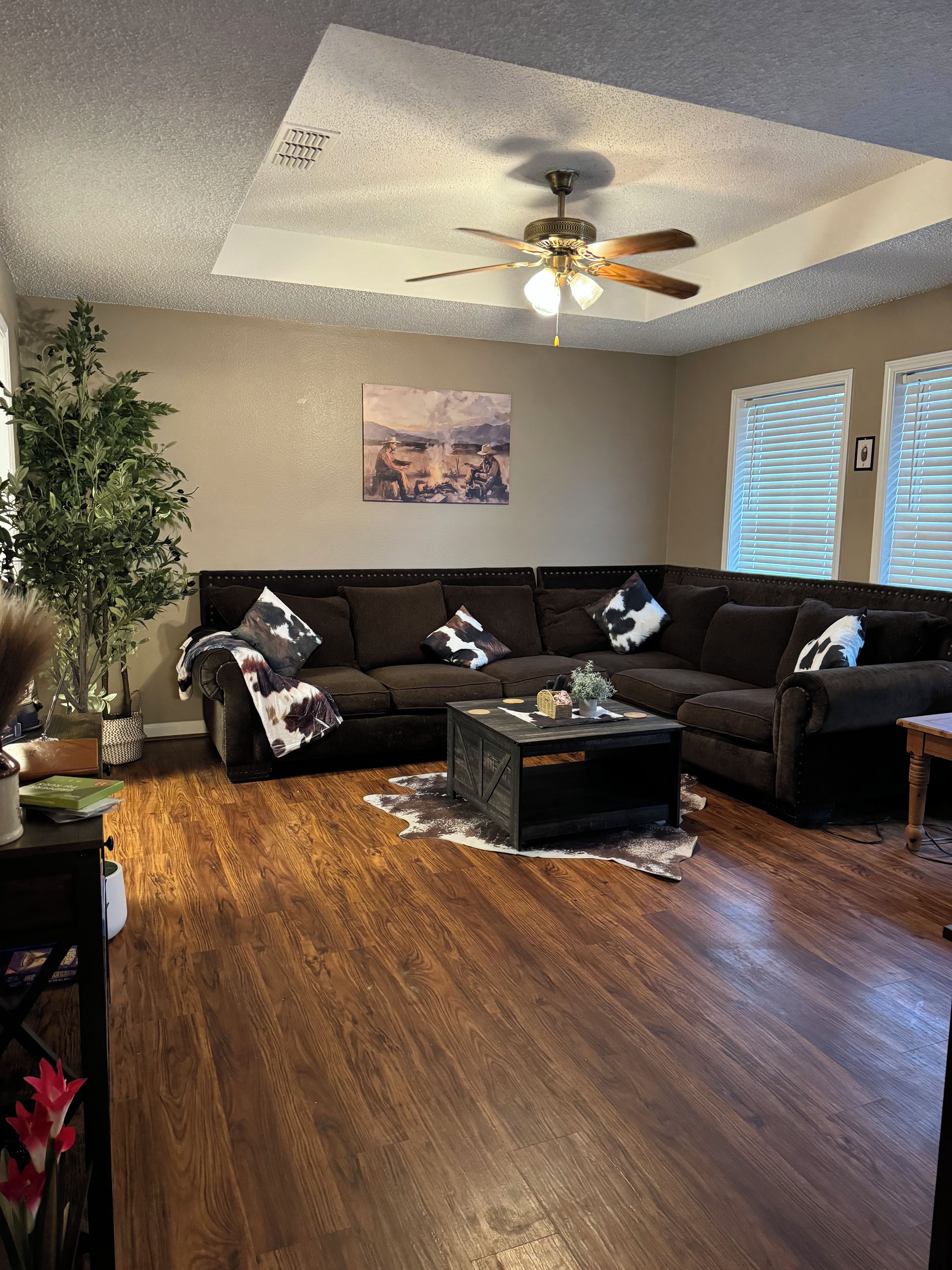 A living room with a dark brown sofa, a coffee table, a ceiling fan, and a painting on the wall.