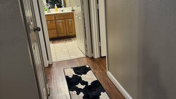 A hallway with wooden flooring, a black and white rug, and a kitchen area with wooden cabinets and a countertop.