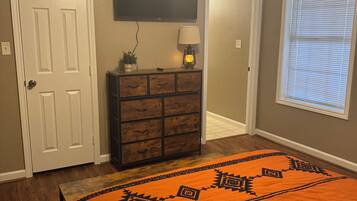 A bedroom with a bed, a dresser, a television, and a window with blinds.