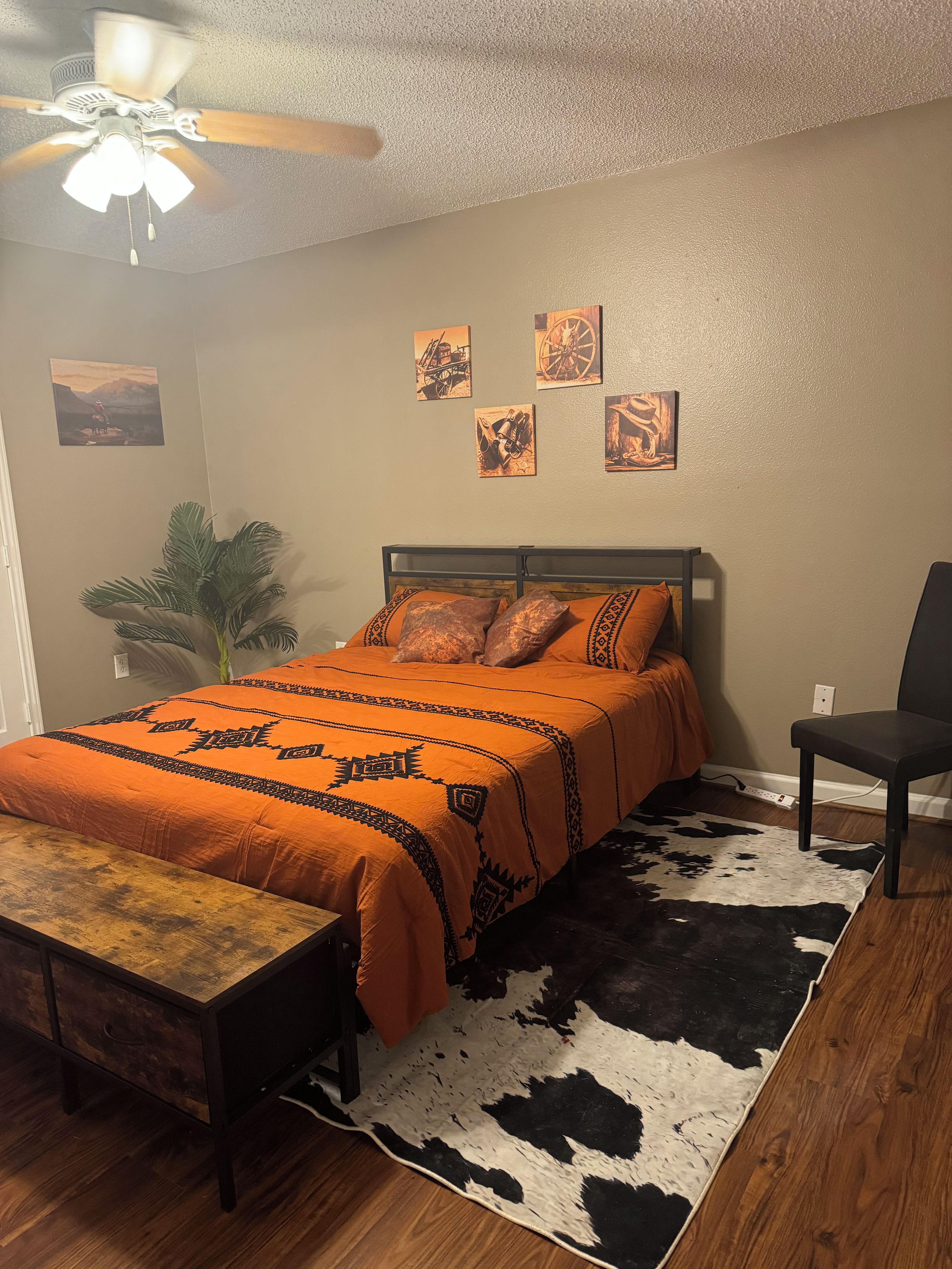 Une chambre à coucher comprenant un lit, une chaise, un ventilateur de plafond et des œuvres d’art murales.