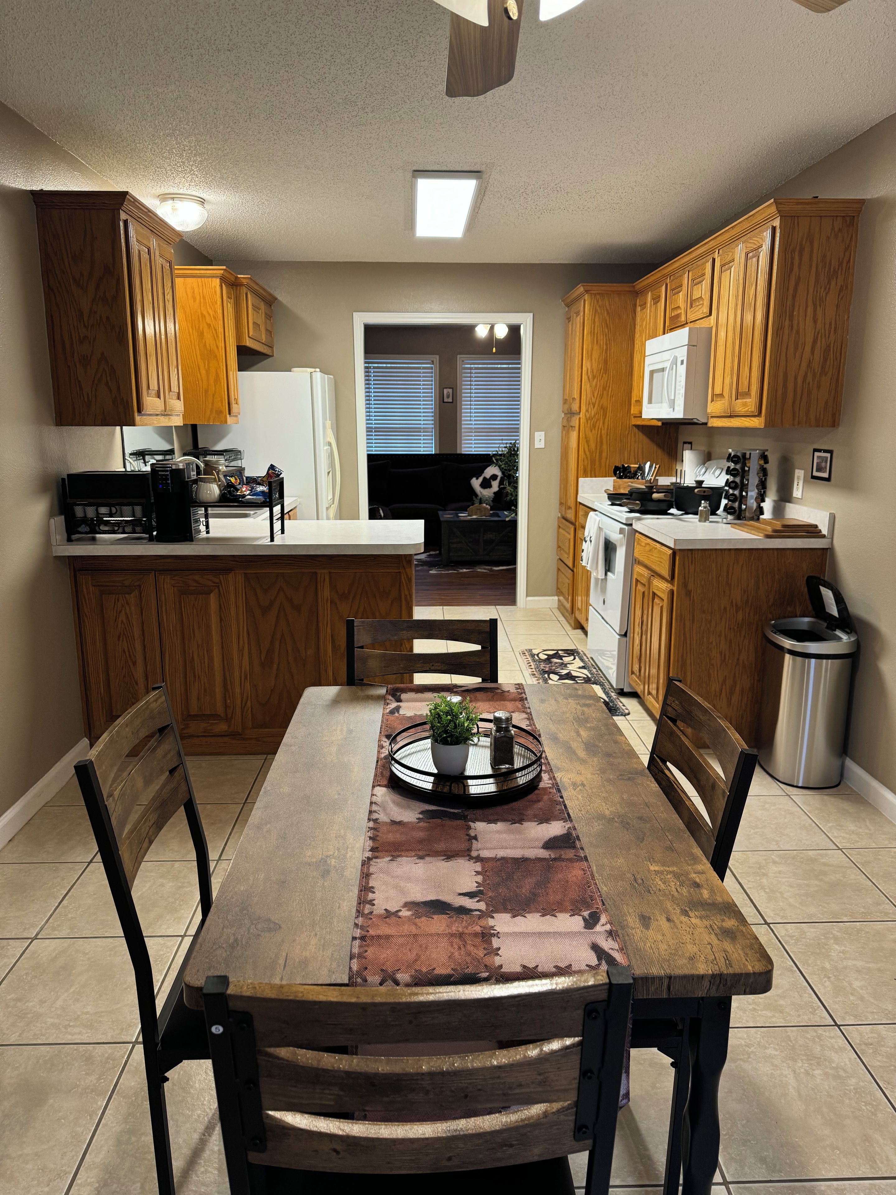 A kitchen with wooden cabinets, a dining table with chairs, and a view into the living area.