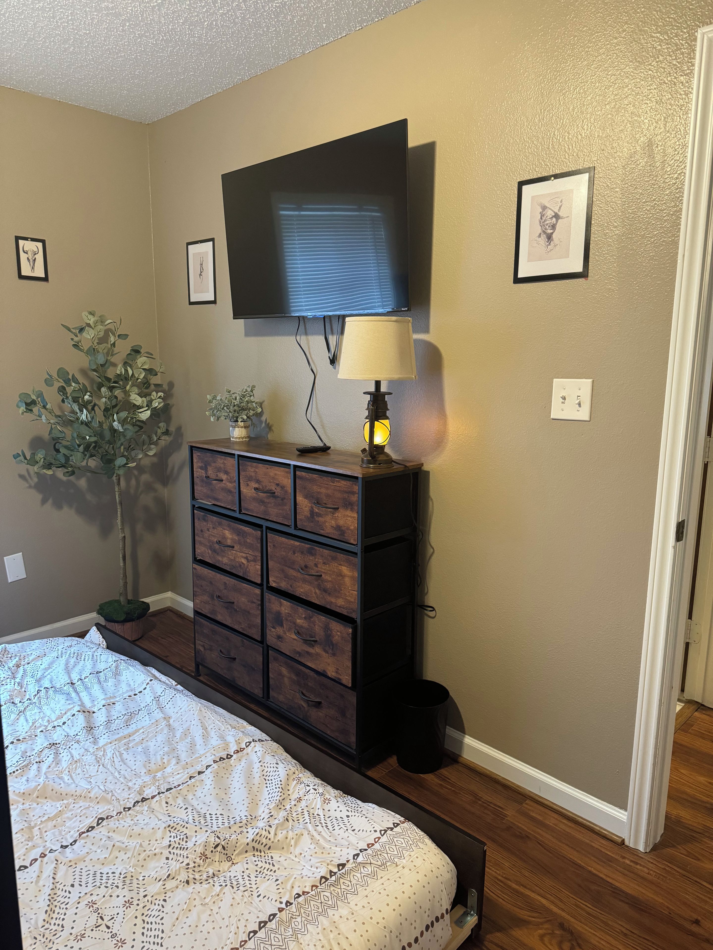 Une chambre à coucher comprenant un lit, une commode, un téléviseur et une lampe fixée au mur.