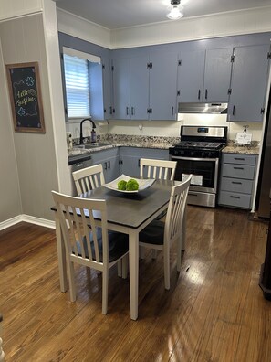 A kitchen with grey cabinets, a black stove, and a dining table with chairs. - Hillside Hideaway 3 Bed 3 Bath home stocked with all the comforts of home (Natchez)