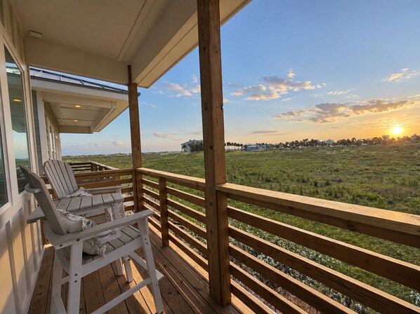 Una terraza de madera con dos sillas y una mesa, con vistas a un campo cubierto de hierba y un atardecer.