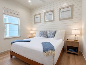Un dormitorio con una cama grande, dos mesitas de noche, un buró y tres marcos con fotografías colgados en la pared.
