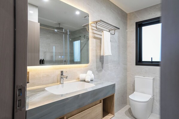 A modern bathroom with a large mirror, a dual sink vanity, a toilet, and a window. - Serene suites (Hamilton)