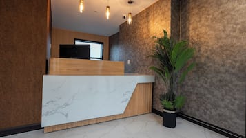 A reception area with a marble counter, wooden paneling, a potted plant, and pendant lighting.