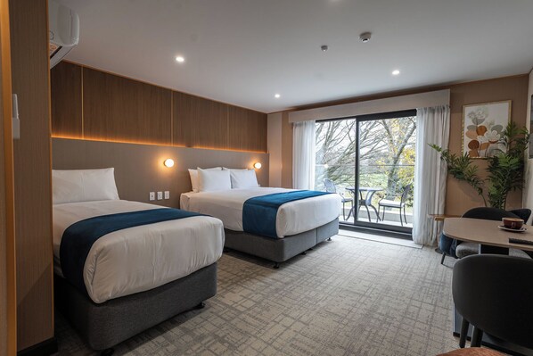 Una habitación de hotel con dos camas, zona de comedor y vistas al exterior.