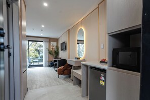 A modern kitchen with a built-in microwave, a refrigerator, and a television. There is a seating area with a table and chairs, and a large window providing a view of the outdoors. - Serene suites (Hamilton)