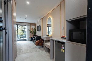 Una cocina moderna con microondas incorporado, refrigerador y televisor. Hay una zona de estar con mesa y sillas, y un ventanal con vistas al exterior.
