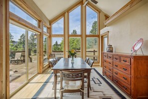 A spacious dining area with a large wooden table and chairs, a wooden cabinet, and large windows offering a view of the outdoors. - Fall Escape Special: 15% Discount Ends Nov 30! Must book by Oct 18 (Pagosa Springs)
