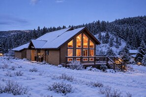 A log cabin with a large central window, surrounded by snow-covered ground and trees. - Fall Escape Special: 15% Discount Ends Nov 30! Must book by Oct 18 (Pagosa Springs)