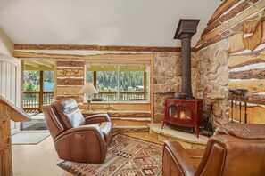 A log cabin interior with a stone fireplace, leather recliner, and a view of the forest through large windows. - Fall Escape Special: 15% Discount Ends Nov 30! Must book by Oct 18 (Pagosa Springs)
