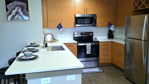 A modern kitchen with a central island, stainless steel appliances, wooden cabinets, and a ceiling light fixture. - Prime 1-bedroom apartment in Uptown Charlotte with Pool and gym (Charlotte)